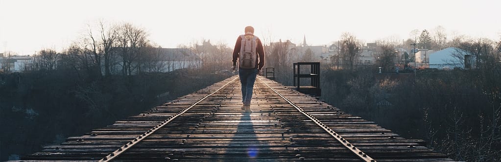 Man walking on train tracks toward sun