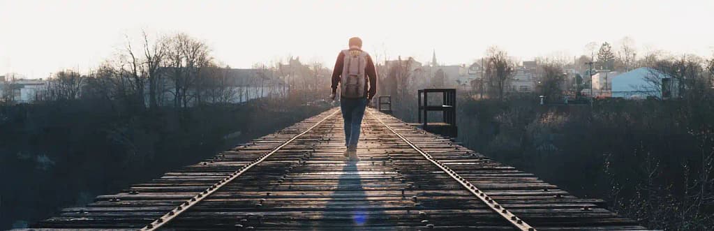 Man walking on train tracks toward sun