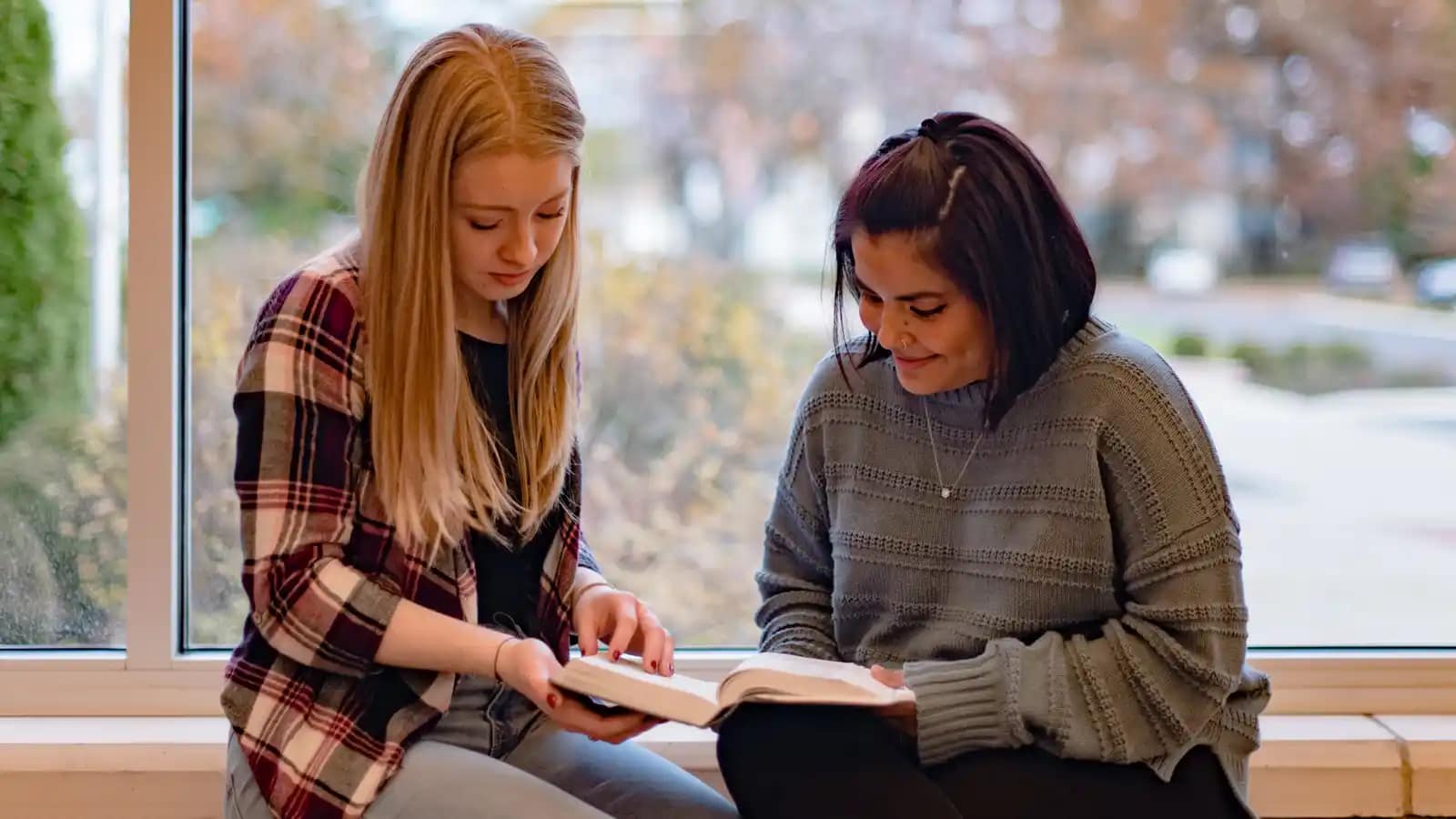 On-Campus-Biblical-Studies Two students sitting by a window, reading the Bible.