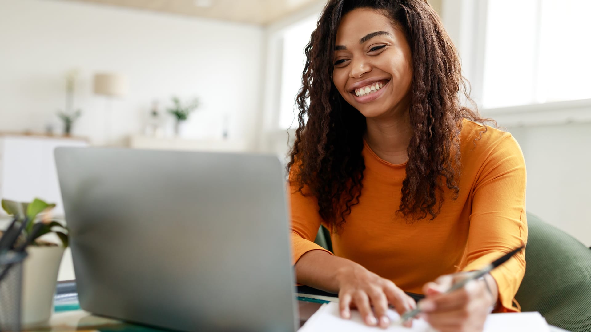 Academic-Support-Center Happy Grace Online Student working on a laptop and writing in a notebook.