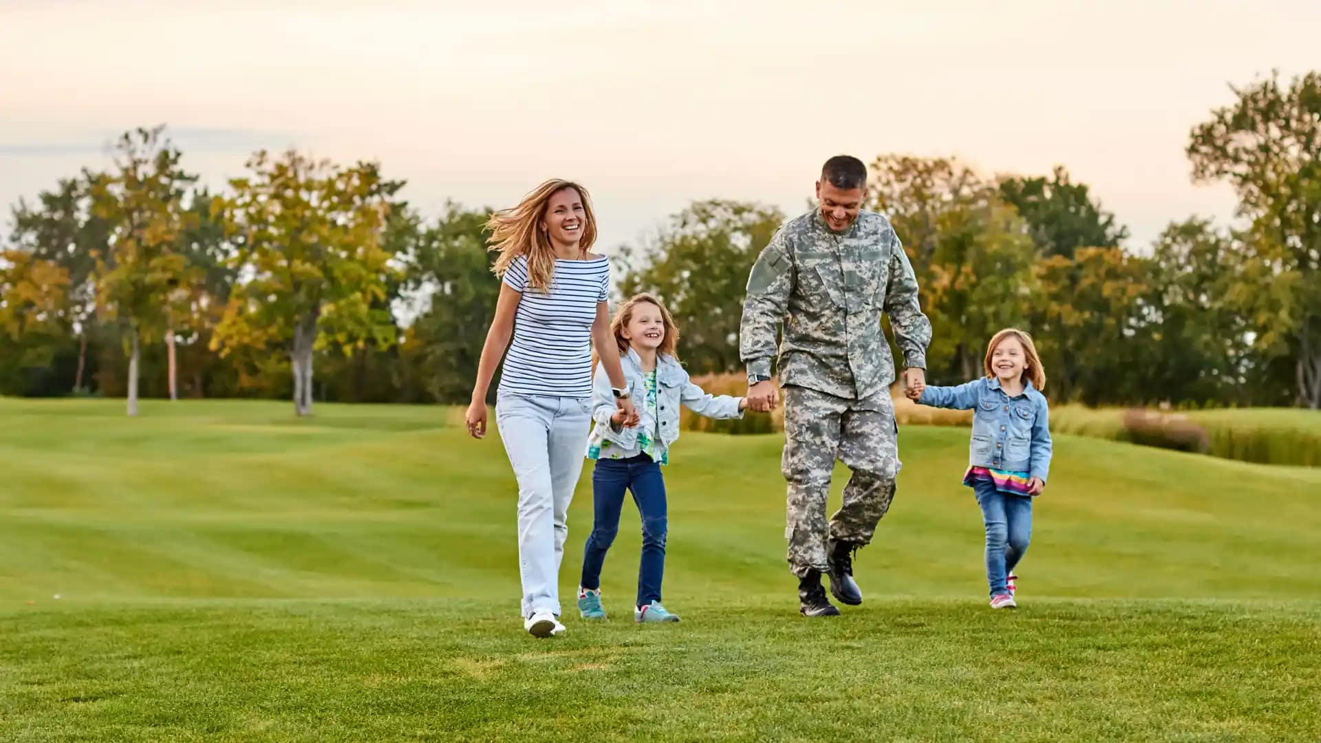 Military-Assistance-Contact Military student family walking hand in hand through a field of grass.