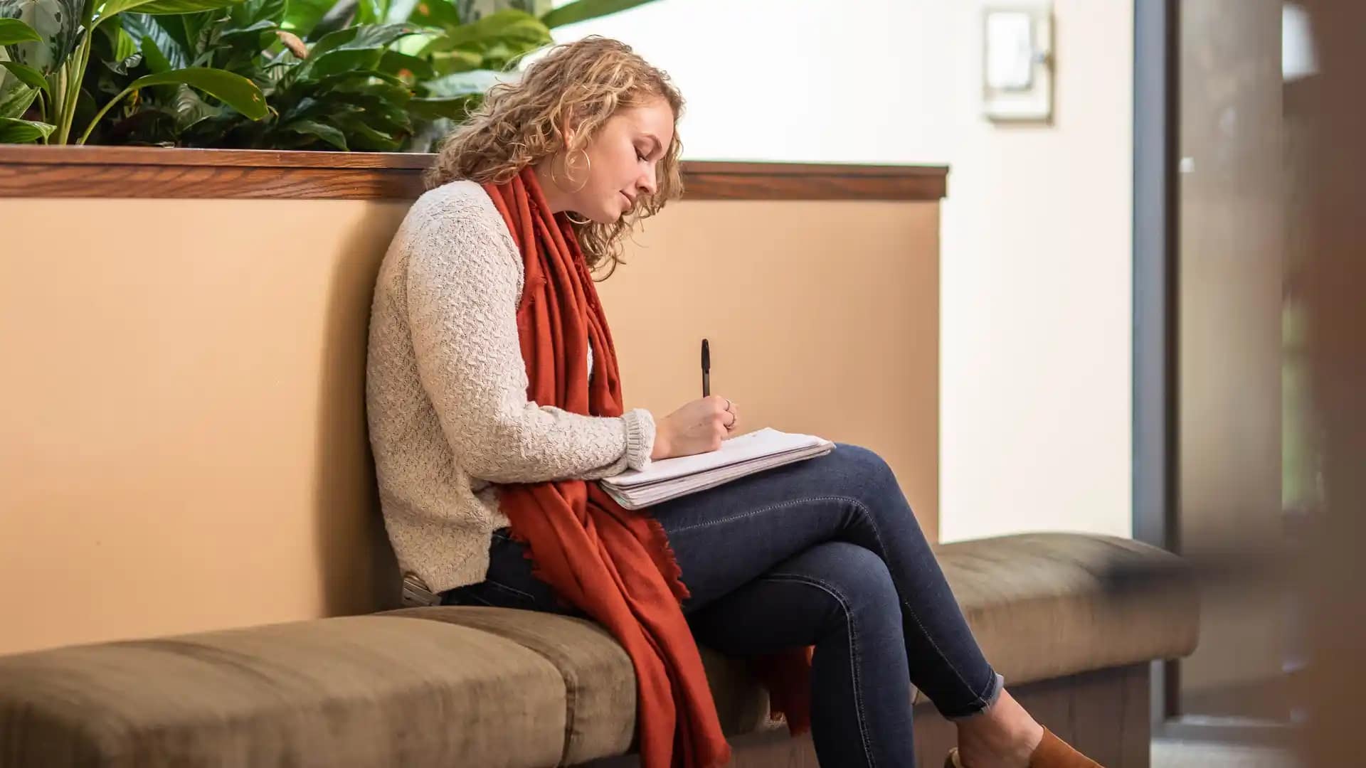 A Grace Student sitting on a bench seat and writing in a notebook in the Student Commons.