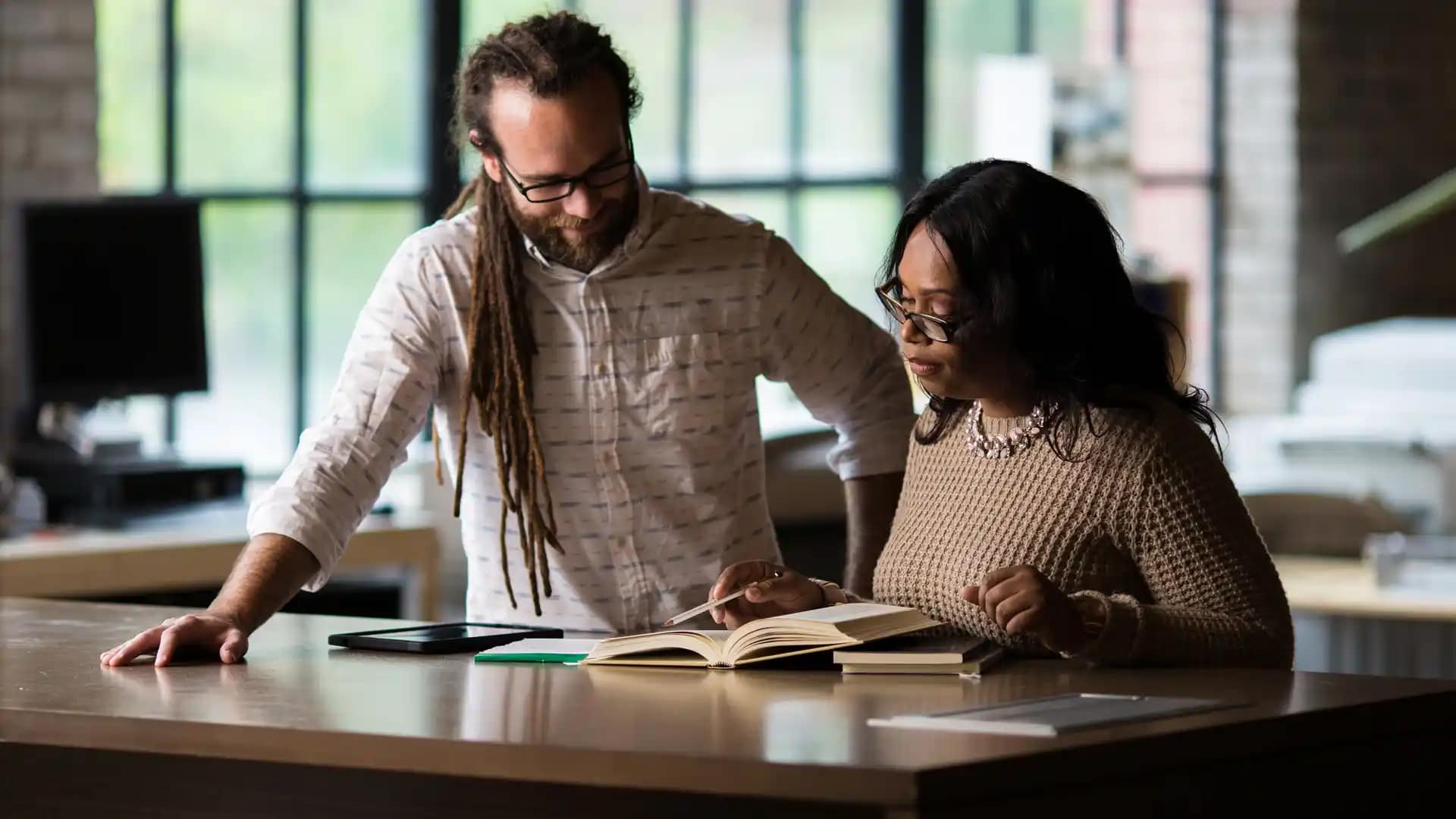 Online-Graduate-Programs Two Grace Graduate Students standing next to a desk looking at a book.