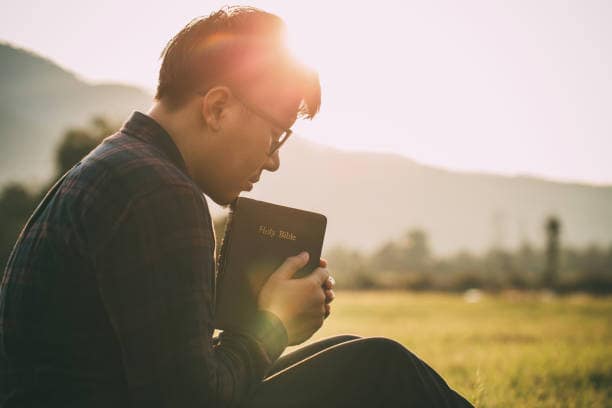 man-praying-on-the- holy-bible-in-a-field-during-beautiful-sunset