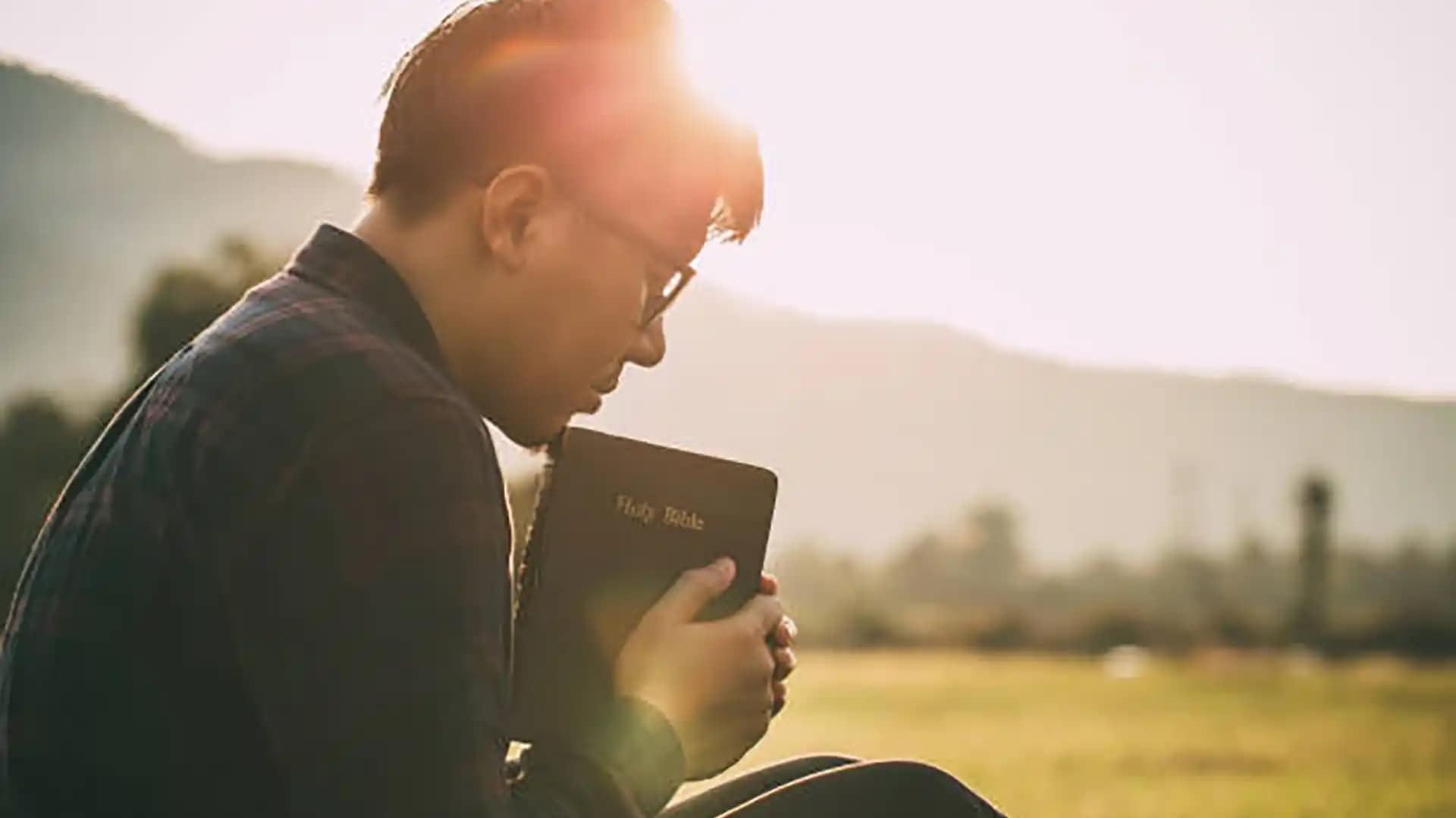 man-praying-on-the- holy-bible-in-a-field-during-beautiful-sunset